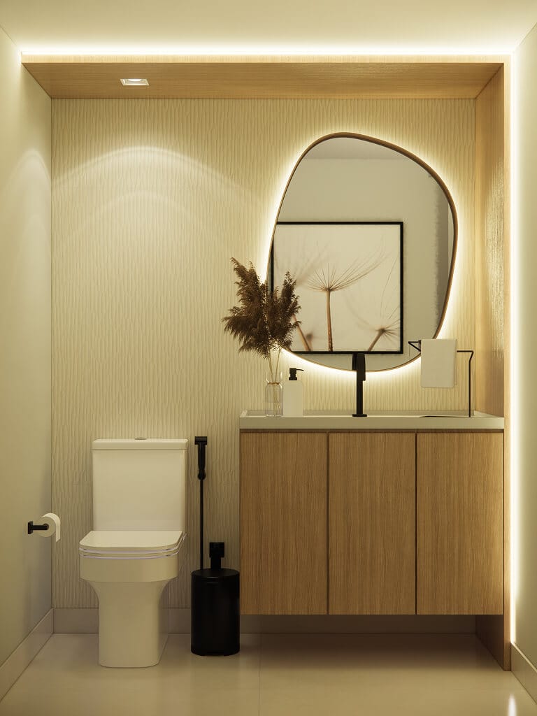Banheiro moderno com vaso sanitário branco, pia de madeira clara, torneira preta, espelho oval com iluminação de fundo e um vaso com plantas secas sobre a bancada. Uma obra de arte emoldurada está pendurada na parede, refletida no espelho.